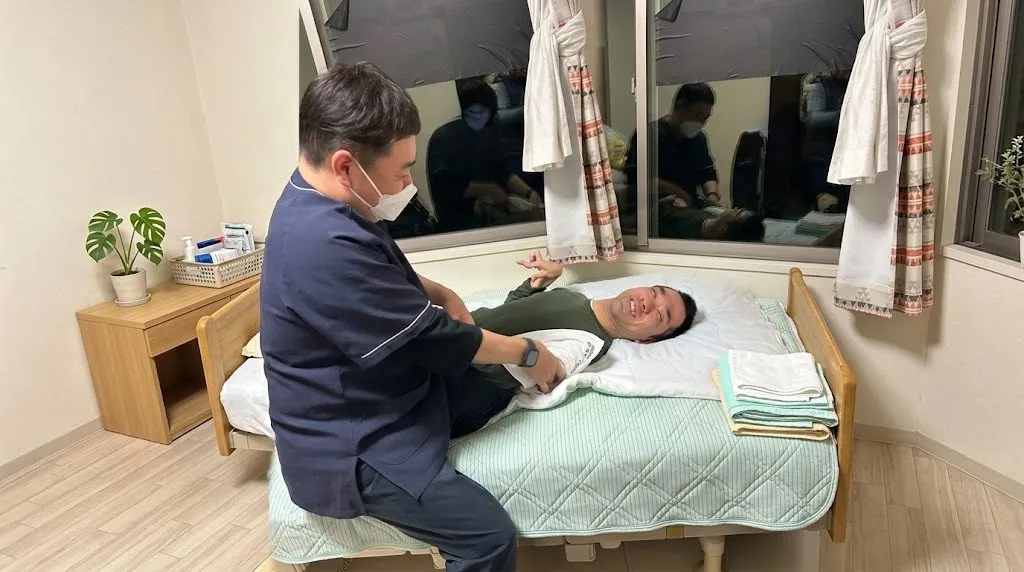 訪問マッサージでベッドの上の利用者様の腕をほぐすスタッフ
